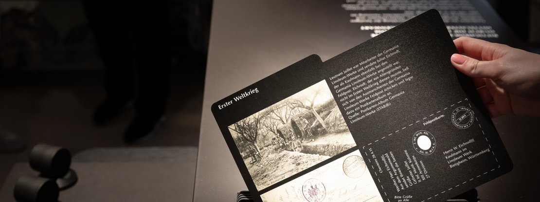 VISUELL Scenography: Permanent exhibition at Hornmoldhaus: Detailed view of an interactive folding map with the heading "First World War", historical photograph and explanatory text. A hand holds the unfolded element above a black exhibition table with an integrated listening station.