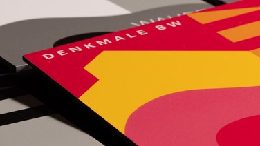 VISUELL Kommunikationsdesign: Detailaufnahme der farbigen Denkmalplakette des Landesamts für Denkmalpflege mit dem Schriftzug „Denkmale BW"